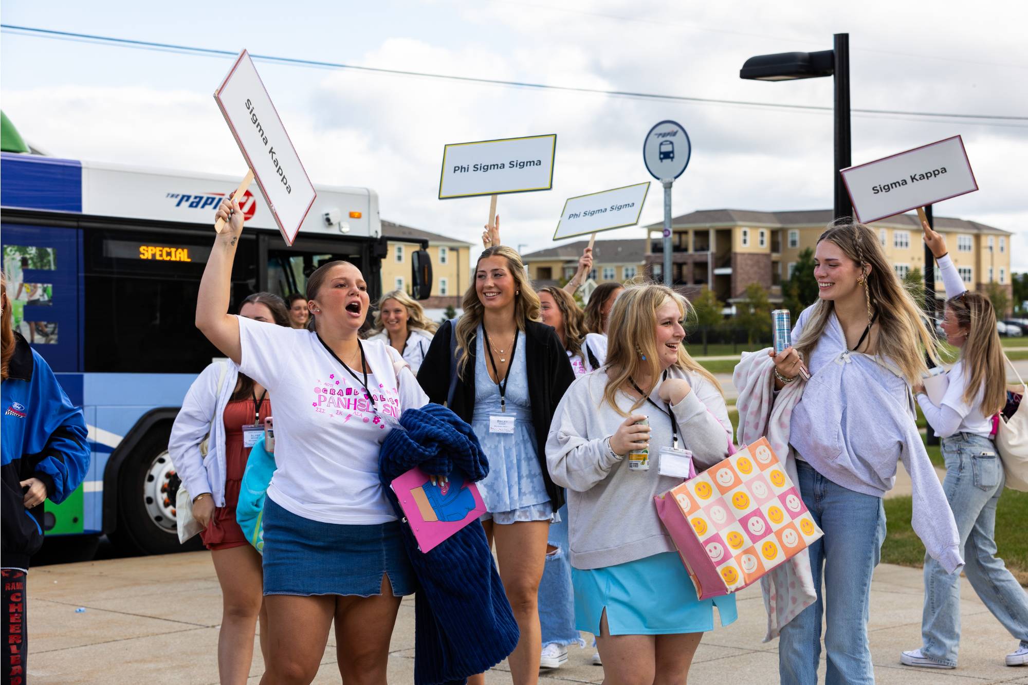 A group sorority women holding chapter signs getting off bus
